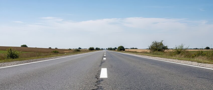 Low angle shot of a long straight asphalt road stretching towards the horizon in a rural landscape under a clear blue sky. Perfect for travel and journey concepts.