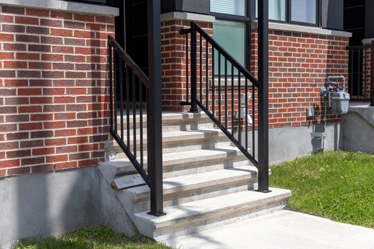 Concrete steps with black metal railing leading to brick house. Entrance and porch of residential building. Exterior detail of townhouse entryway.