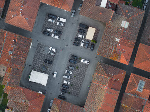 Aerial view of a town square with parked cars and red-tiled rooftops featuring traditional scalloped paving patterns Castelfranco Piandisco, Tuscany, Italy.