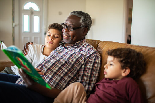 Grandfather reading to grandchildren on sofa at home