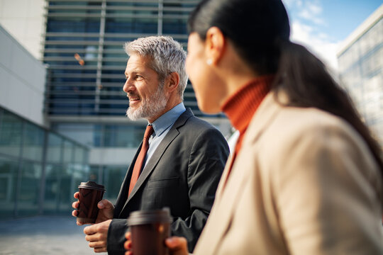 Smiling business colleagues walking with coffee outside modern office