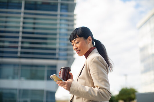 Professional woman using smartphone with coffee outside office building
