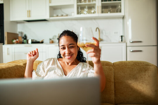 Smiling woman toasting with wine on video call at home kitchen