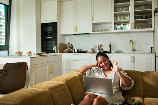 Smiling woman waving on a video call with laptop in modern home kitchen