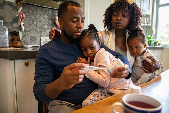 Parents comforting sick children and checking fever in home kitchen