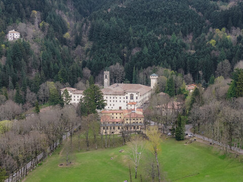 Aerial view of the historic Vallombrosa Abbey with its prominent clock tower nestled among dense evergreen forests and a lush green meadow in Vallombrosa, Tuscany, Italy.