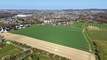 Aerial view showing german city menden with houses, fields, and forest merging under blue sky © Karina