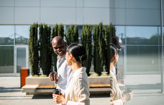 Coworkers walking with coffee outside modern office building