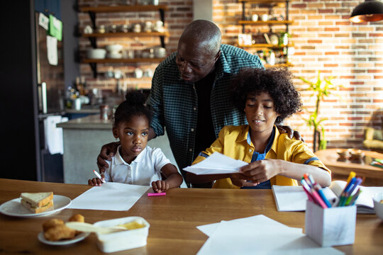 Grandfather helping grandchildren with homework at kitchen table