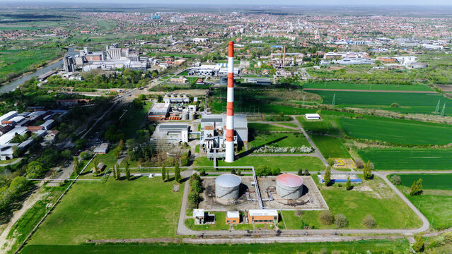 Aerial view of the red and white chimney standing tall amid the industrial landscape, juxtaposed against the green fields, Zrenjanin, Vojvodina, Serbia.