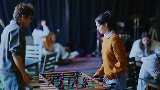 Young students engage in a friendly game of foosball in a vibrant recreation room. They enjoy leisure time and playful competition among friends.