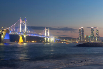 Fototapeta premium Gwangan Bridge light up against skyscraper and motion wave at dusk, Busan
