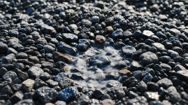 Close-up of water dropping onto a collection of wet rocks and pebbles with a pool of water in a natural setting.