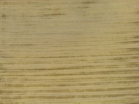 Aerial view of a plowed agricultural field with parallel horizontal furrows and earthy textures in Castelfranco Piandisco, Tuscany, Italy.