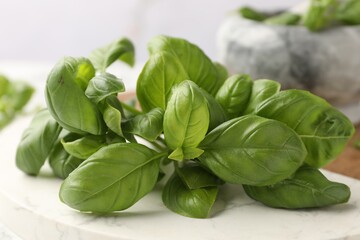 Fototapeta premium Fresh basil leaves on white board against blurred background, closeup