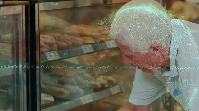 Senior man in light polo leaning toward glass display at bakery, pointing at donuts and labels