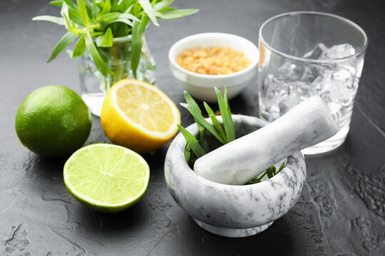 Mortar with pestle and ingredients for estragon lemonade on black table, closeup