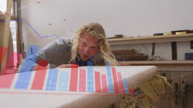 Shaper in shop running hand along surfboard blank, checking finish while red blue charts responding