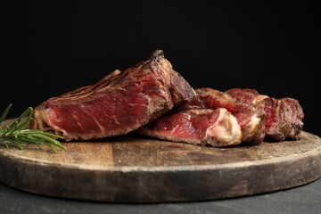 Fototapeta premium Pieces of tasty beef steak with rosemary on table against black background, closeup