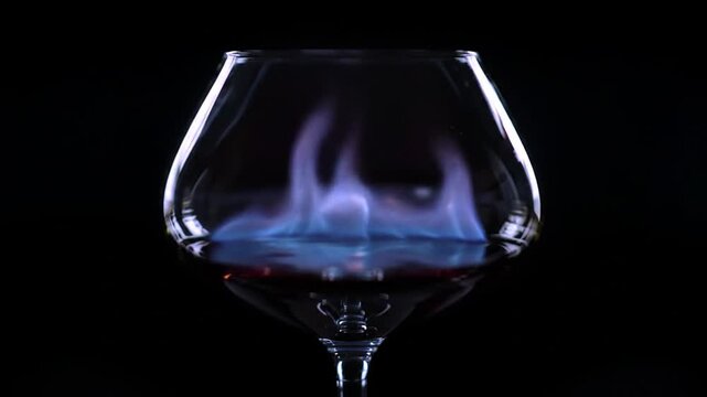 Flaming cognac drink in snifter glass over black background