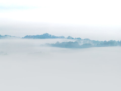 Aerial view of Le Balze del Valdarno shrouded in thick white fog with treetops emerging from the misty clouds in Castelfranco Piandisco, Tuscany, Italy.