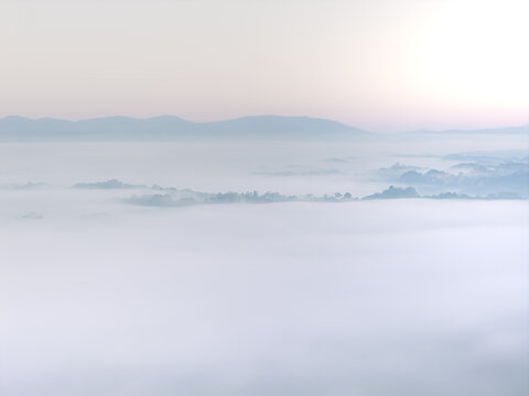 Aerial view of Le Balze del Valdarno covered in thick white fog with distant mountain ridges under a soft morning sky in Castelfranco Piandisco, Tuscany, Italy.