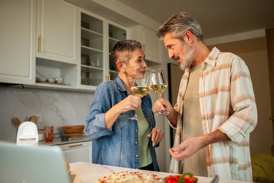 Senior couple toasting white wine in cozy home kitchen