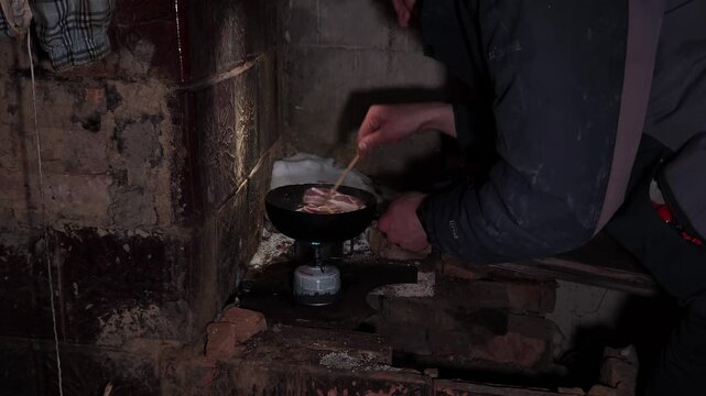  Cooking meat in a frying pan over a gas burner in a hut
