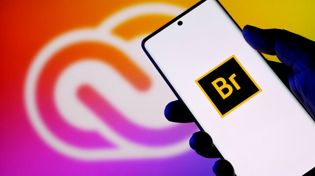 Closeup of a hand holding a smartphone displaying the adobe bridge app icon