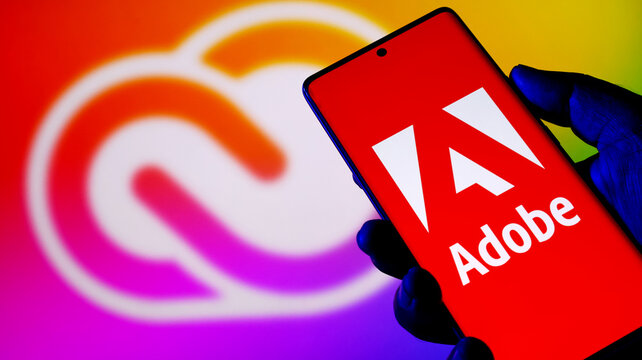 Hand holding smartphone with adobe logo on screen against creative cloud background