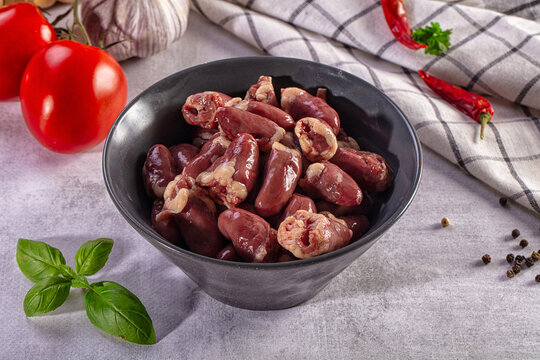 Raw chicken hearts in a black bowl with fresh ingredients like tomatoes, garlic, basil and spices