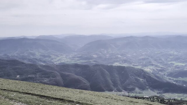 Panoramica montana con colline verdi in primo piano e catene montuose che sfumano nella foschia. Un paesaggio naturale ampio e suggestivo