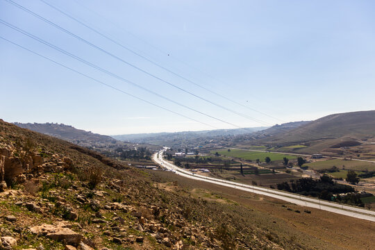 Wide landscape of Sukhna street highway cutting through the rural valley and hills in Zarqa Governorate Jordan under clear blue sky.