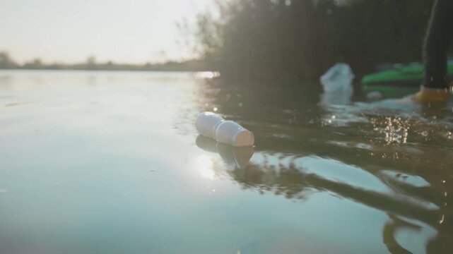 Volunteer rescues plastic, Tranquil lakeside setting as volunteer gathers floating trash amid shimmering ripples