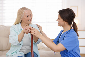 Fototapeta premium Smiling care worker supporting senior woman with walking cane at nursing home
