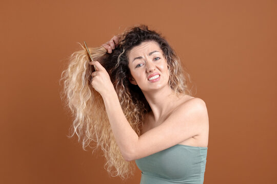Unhappy woman trying to brush her tangled hair on brown background