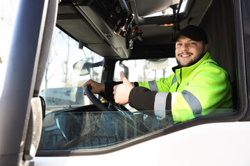 Naklejka premium Happy young driver showing thumbs up and sitting in modern truck