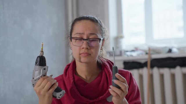 Woman Assembling Furniture Adjusting Drill And Studying Screw Head, Intimate Closeup, Neutral Renovation Interior, Quiet Frustration Turning Into Problem Solving, Tools On Nearby Table