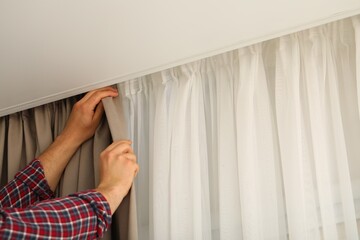 Man hanging window curtain in room, closeup. Space for text © New Africa