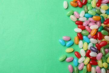 Obraz premium Delicious colorful candies on green background, flat lay. Space for text