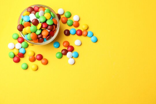 Delicious colorful candies in glass bowl on yellow background, flat lay. Space for text