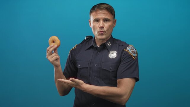 Police officer man holds donut in right hand and presents it with palm up in studio; playful public service.