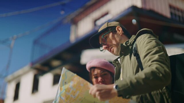 A diverse couple of tourists are studying a map intensely while navigating a city street. They are exploring an urban area, planning their route with a paper map.