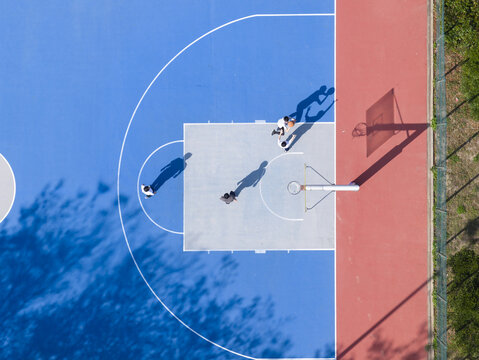 Aerial view of people playing on a colorful blue and red basketball court with long shadows on a sunny day Taiwan.