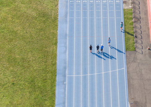 Aerial view of athletes running on a blue athletics track with numbered lanes next to a green lawn in Taiwan.