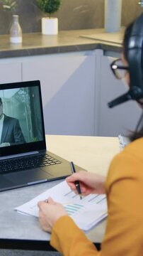 Adorable considerate cvalified 35-aged female office manager in stylish jacket using headphones has online meeting with bearded man-partner and talking about details of financial reports