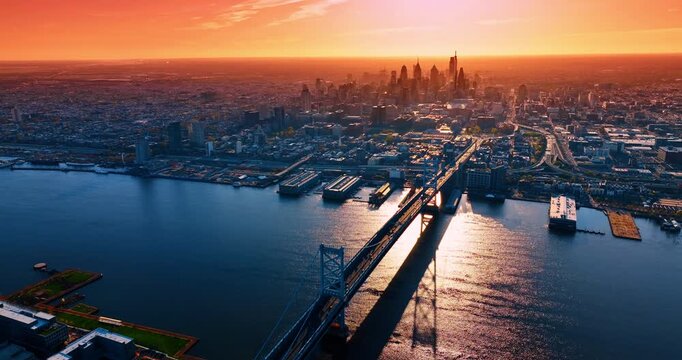 Approaching the Benjamin Franklin Bridge over the Delaware River in Philadelphia, Pennsylvania, USA. Vast panorama of the city against orange sky. Aerial view.