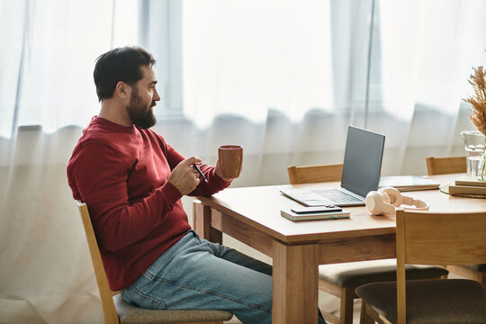 Relaxing at home, a handsome man enjoys coffee while working on his laptop in a cozy space