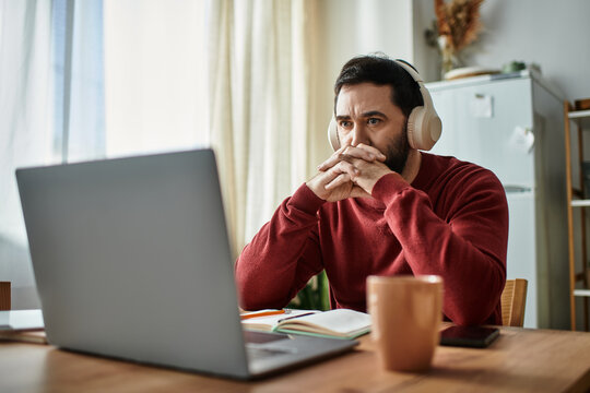Focused adult man at home engages in deep thought while working on his laptop