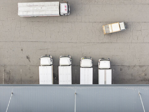 Aerial view of a logistics center with white trucks parked at loading docks and a vehicle moving across cracked asphalt Taiwan.
